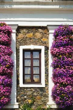 Charming window on a rustic stone wall framed by vibrant blooming flowers a.. Stock Photos