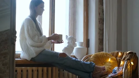 Charming woman drinking tea while sitting on the windowsill Stock Footage 146941683