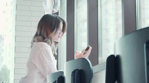 Charming woman smiling at the camera while using her smartphone in a cozy coffee Stock Footage 311985043