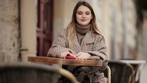 Charming young blonde girl using mobile phone while sitting at the cafe outdoors Stock Footage 151899206