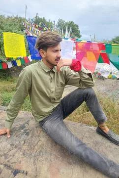 A charming young guy looking sideways while sitting on rock with the background  Stock Photos