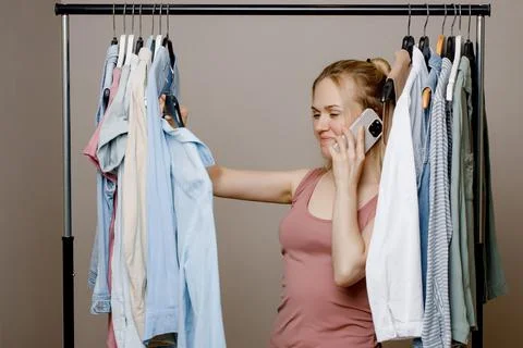 Charming young lady is talking on a mobile phone among fashionable clothes in Stock Photos