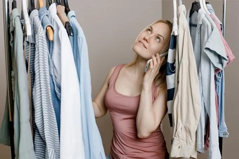 Charming young lady is talking on a mobile phone among fashionable clothes in Stock Photos