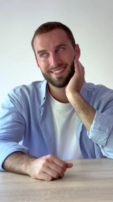 Charming young man with a beard and blue eyes smiling at the camera, sitting Stock Footage 346600659