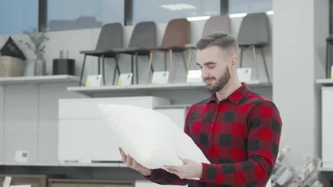Charming young man joyfully selecting a cozy pillow at a stylish furnishings Stock Footage 311672697