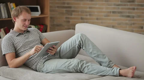 Charming young man relaxing on couch using touchpad looking at camera  動画素材 34278070