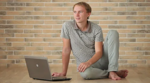 Charming young man sitting on floor with laptop looking at camera and smiling Stock Footage 34278083