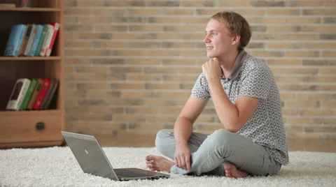 Charming young man sitting on floor using laptop and smiling Stock Footage 34278092