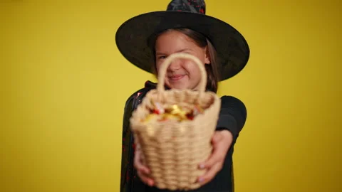 A Charming Young Witch Holding a Colorful Candy Basket on a Bright Yellow Stock Footage 315412341