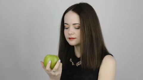 Charming young woman eats a green apple and smiles Stock Footage 87310089