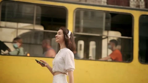 Charming young woman walking down the street with headphones listening to music Stock Footage 249407045