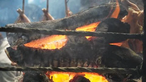 Charred logs burn while chickens roast in smoky rustic setting Stock Photos