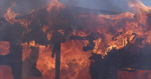 Charred outline of house in flames, chunks of burning debris drop down from the Stock Footage 59534719