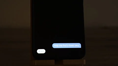 Chat bubbles on an upright smartphone show a user asking for a fresh idea, an AI Stock Footage 347516493