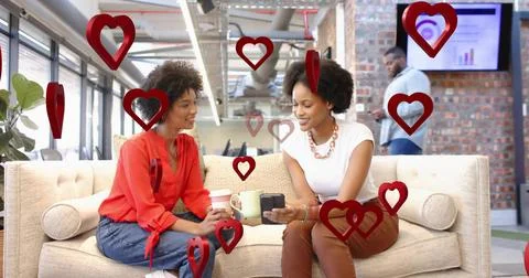 Chatting pair wearing red blouse and white top holding coffee, device on offi Stock Photos