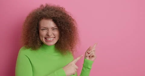 Check this out. Positive curly haired woman points index fingers at upper right Stock Footage 151623482