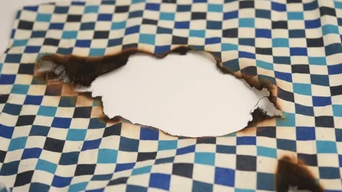 Checkered fabric with a hole and burn marks shown up close Stock Footage 329084043
