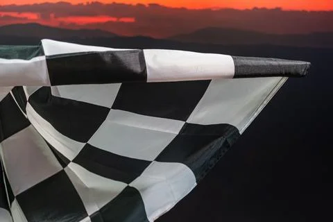Checkered flag blowing in wind, silhouetted mountains at sunrisesunset, rea.. Stock Photos