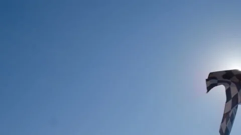 Checkered racing flag waving against the sun and a blue sky Stock Footage 158928703