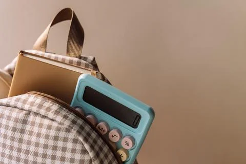 Checkered school backpack with notebook and blue calculator in warm light Stock Photos