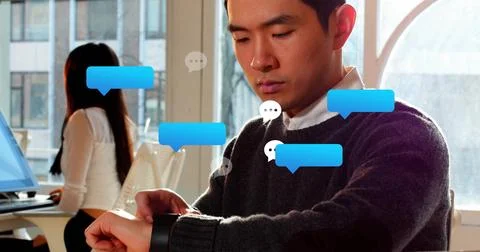 Checking Asian man using watch in dark sweater at desks by windows, chat bubble Stock Photos