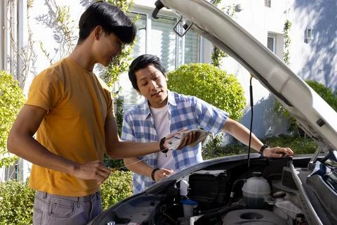 Checking car engine, Asian father and teenage son using smartphone for Fotos de archivo