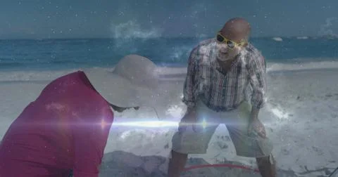 Checking couple responding to sun glare, bending over sand to inspect red hoop, Fotos Stock