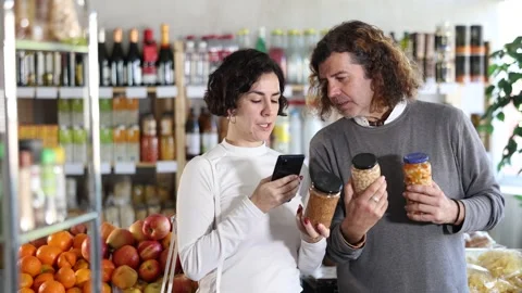 Checking expiration date of beans - wife and husband shoppers scans QR code on Stock Footage 323069875