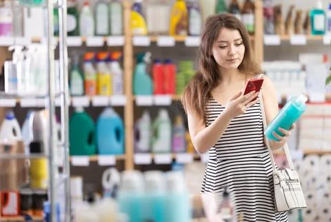 Checking expiration date of shampoo or shower gel - female shopper scans QR code Foto stock