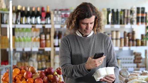 Checking expiration date of yogurt - male shopper scans QR code on label of Stock Footage 346120392