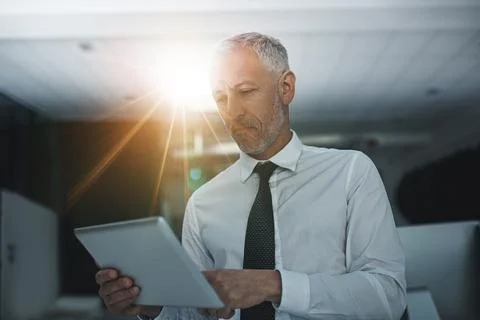 Checking figures in real time. a businessman standing in an office using a Stock Photos