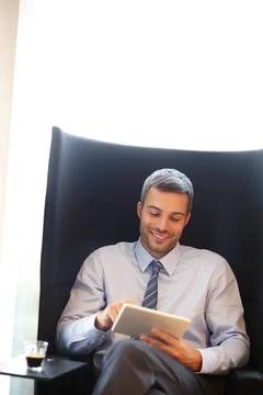 Checking his email. A smiling young businessman using a digital tablet while 写真素材