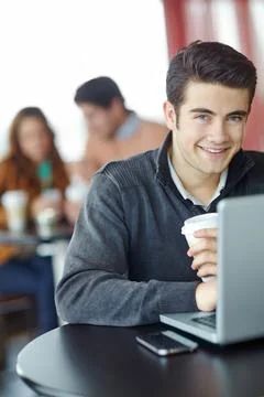 Checking his emails on the go. A handsome young man using his laptop in a coffee Stock Photos