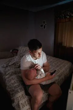 Checking His Phone While Comforting the Baby Fotos Stock