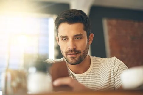 Checking his texts. a young man using his cellphone in a coffee shop. 写真素材