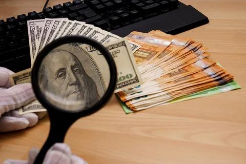 Checking a hundred dollar bill through a magnifying glass. Nearby fifty-euro Stock Photos