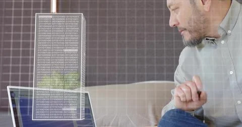 Checking laptop, man on couch in gray shirt holding pen, viewing binary Fotos Stock