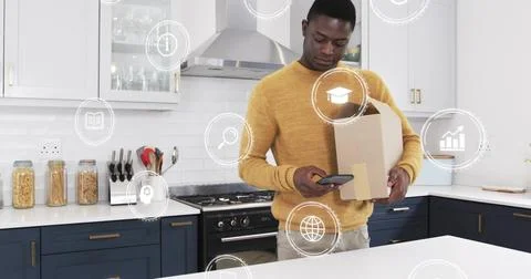 Checking man in mustard sweater using smartphone in home kitchen, holding box Stock Photos