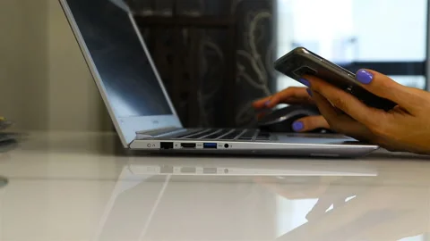 Checking the ordered goods on a laptop with a phone in hand Stock Footage 106013780