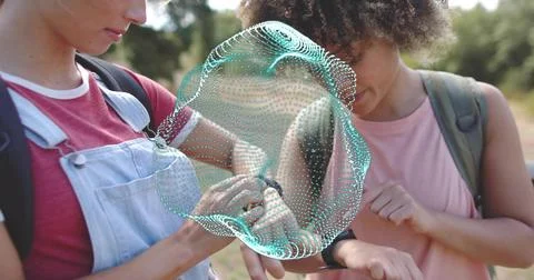 Checking pair inspecting wrist device at park, showing teal hologram, backpacks, Stock Photos