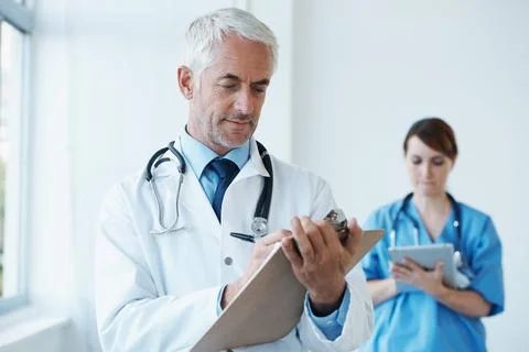 Checking the records using old and new methods. A mature doctor checking records Stock Photos