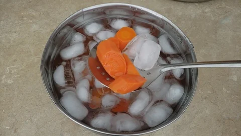 Checking with skimmer blanched slices of carrots being cooling down in ice bath 스톡 동영상 105564882