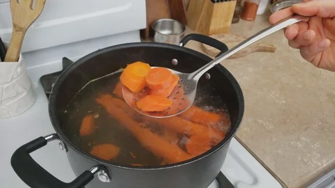 Checking with skimmer thick slices of carrots being boiled in pot 스톡 동영상 105579754