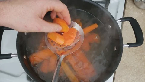 Checking with skimmer whole and sliced carrots being boiled in non stick pot 스톡 동영상 105558518