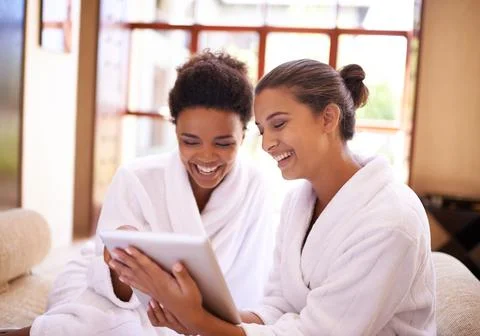 Checking in At the spa. Shot of two friends in bathrobes using a digital tablet Stock Photos