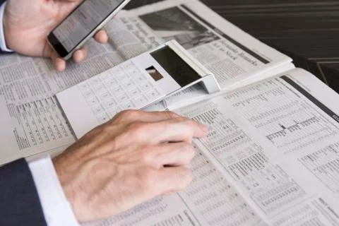 Checking stock market performance using smartphone and newspaper Fotos de archivo