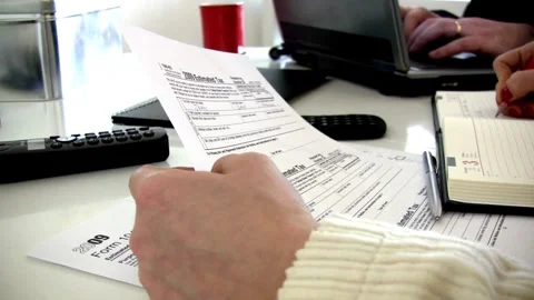 Checking tax forms and using a calculator and pen filling US 1040 tax form .. Stock Footage 272783747