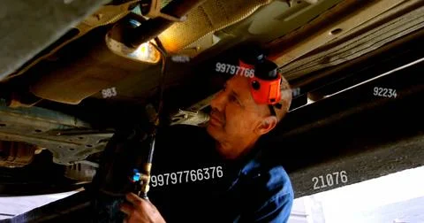 Checking tech in navy work shirt working under vehicle in garage, using orange 写真素材