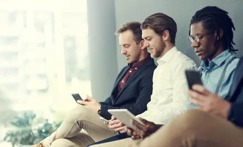 Checking their social platforms while they wait. a group of businessmen using Stock Photos