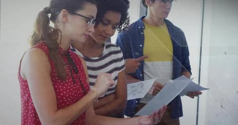 Checking trio leaning over papers near mesh partition, featuring red blouse,  Stock Photos